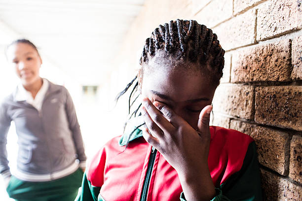 A bullied school girl wipes her eyes as another girl looks on.